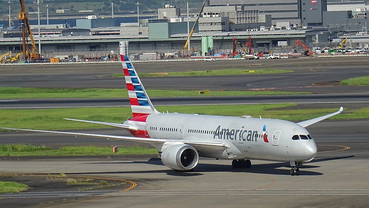 An American Airlines Boeing 787-9 Dreamliner in the airline's silver livery on the runway, seen side-on under a partly cloudy sky
