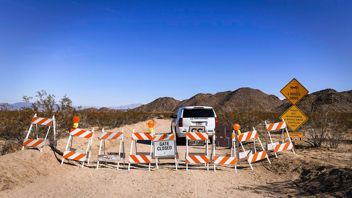 A row of Gate Closed barricades blocking a dirt road at Joshua Tree National Park, with a US Park Ranger vehicle parked behind them