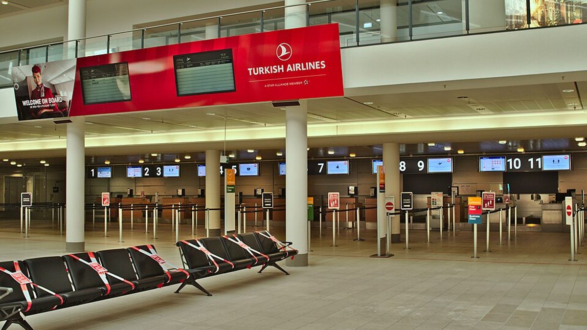 A row of airline check-in counters at an airport terminal, screens showing economy check-in