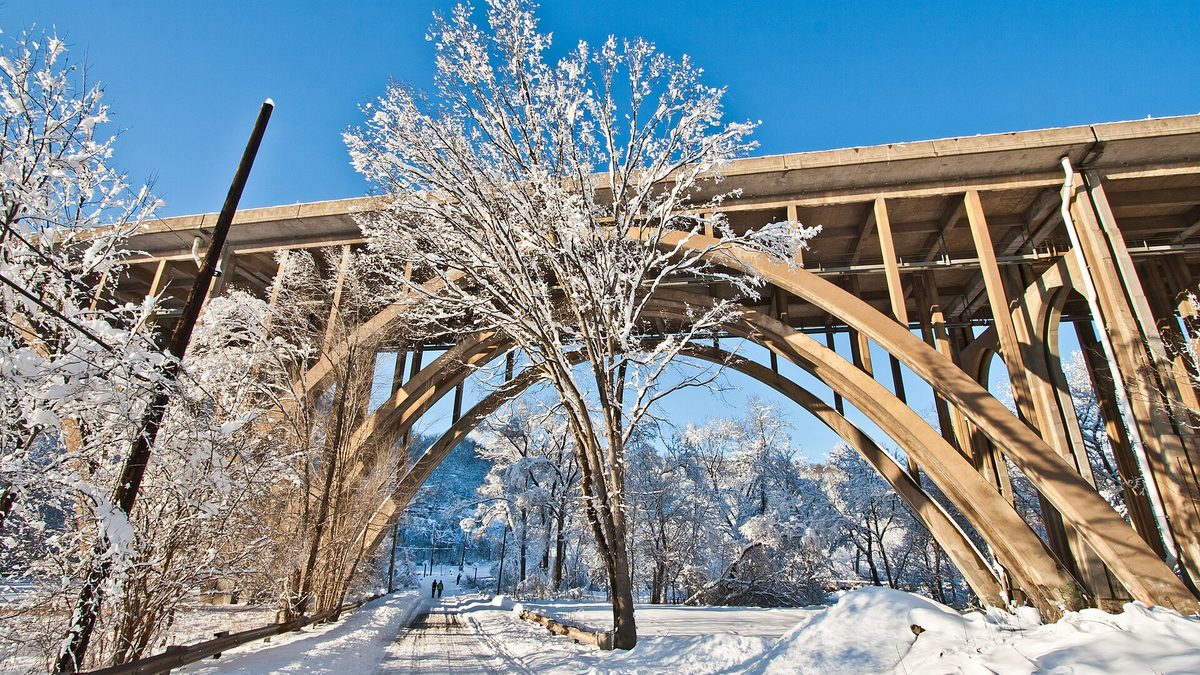 A snow-covered road running beneath the concrete arches of the Commercial Street Bridge in Pittsburgh on a clear winter day