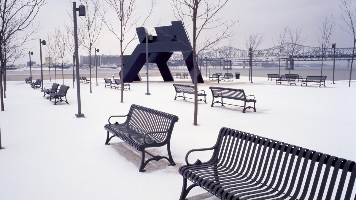 Snow-covered benches and the Gracehoper sculpture at Waterfront Park in Louisville, Kentucky, with the Ohio River bridges in the background