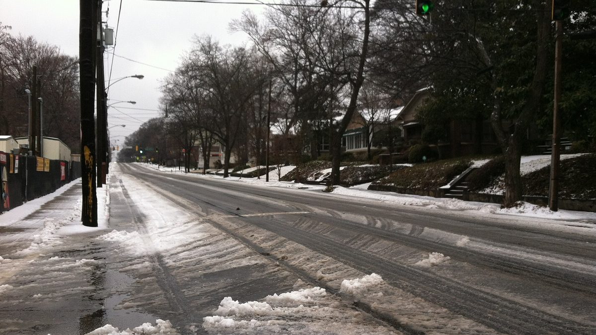 A snow and slush covered residential street in Atlanta, Georgia, with bare trees and a green traffic light overhead